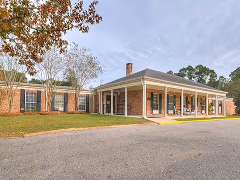 Brick senior living facility with a long covered front entry and lawn.