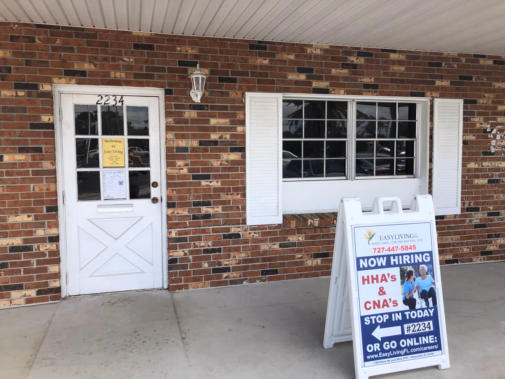 Brick exterior with white door and window, EasyLiving sign, and a Now Hiring sign.