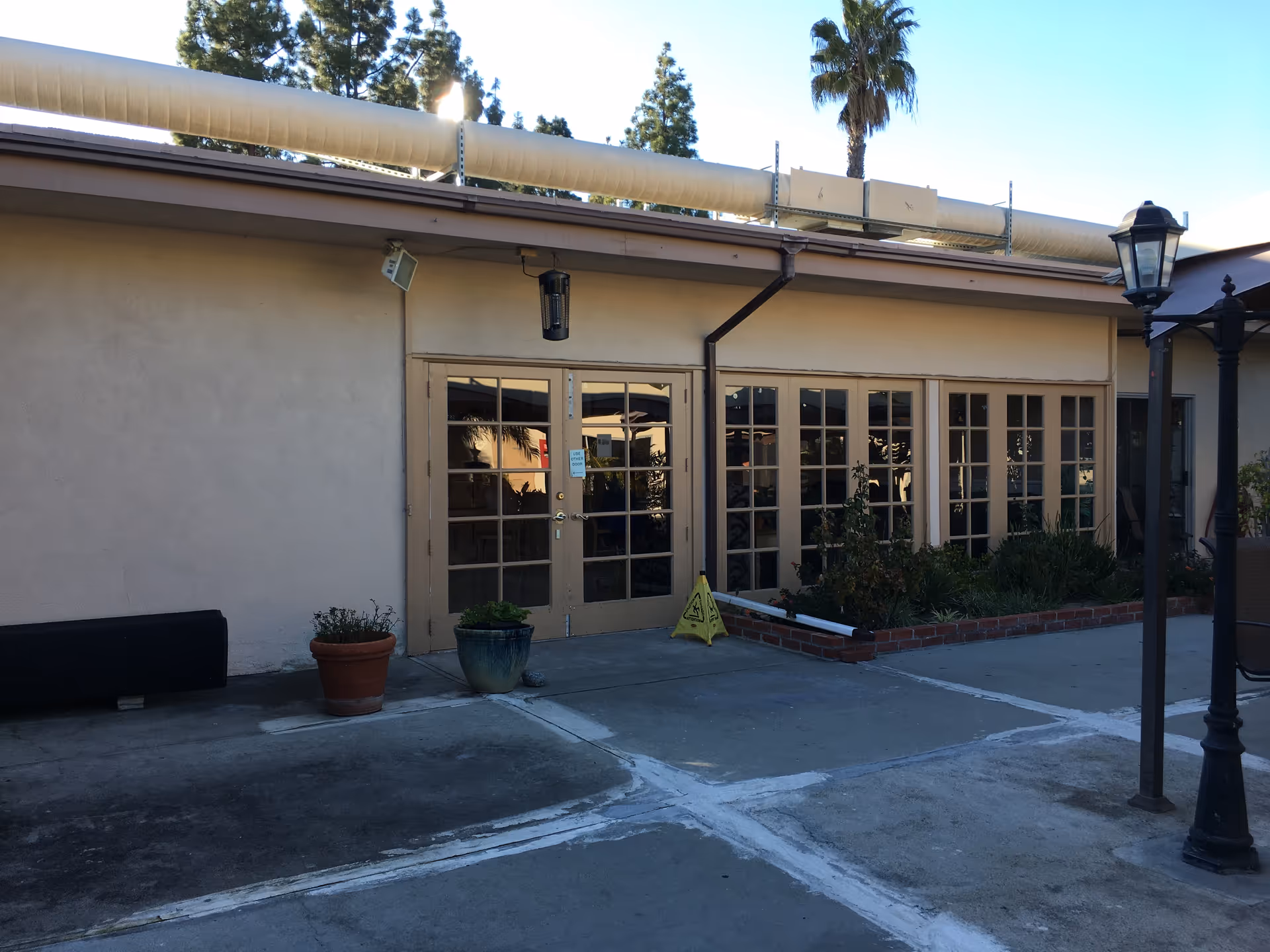 Front entrance of a senior care facility with glass doors, potted plants, and outdoor lighting.