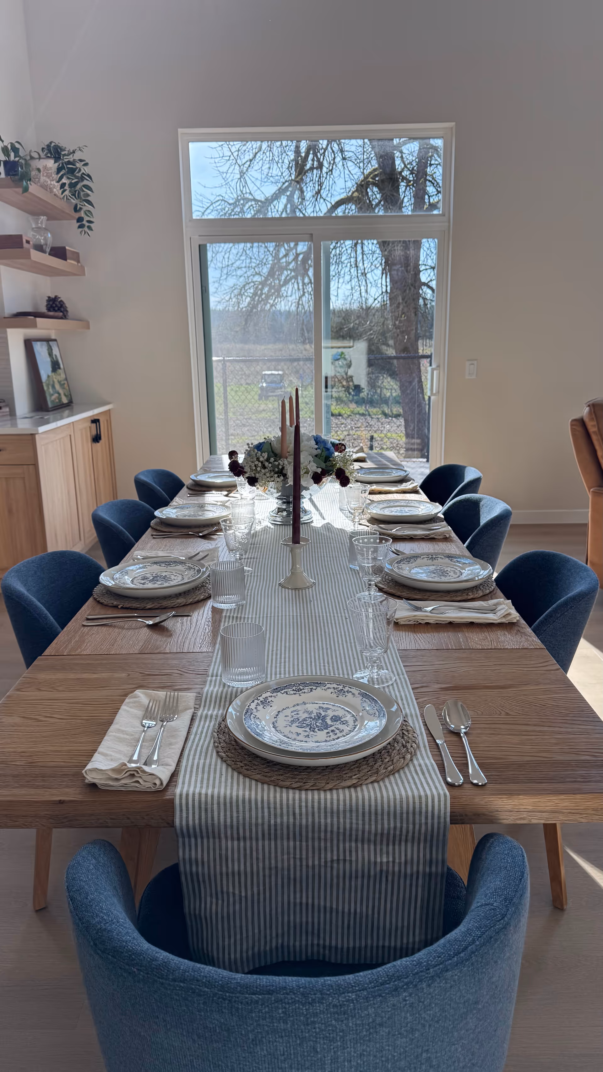 A long dining table set for a meal with blue chairs in a bright dining room.