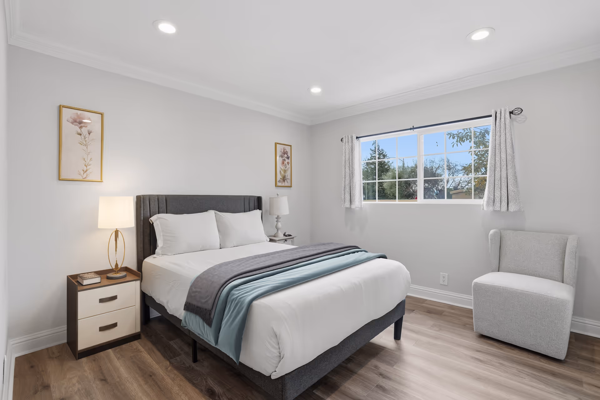 A modern bedroom in a senior living facility with bed, nightstands, and a chair.