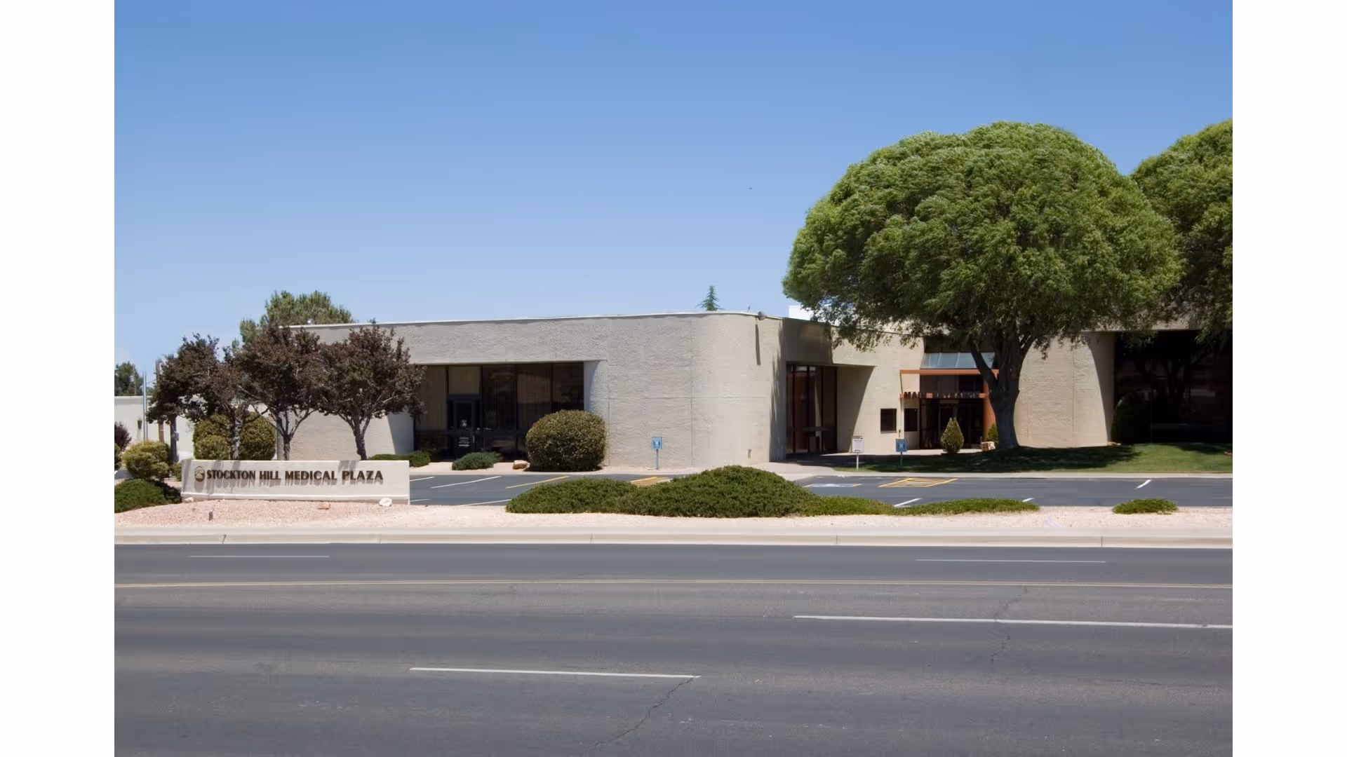 Exterior view of a low-rise medical plaza with a large tree and parking area.