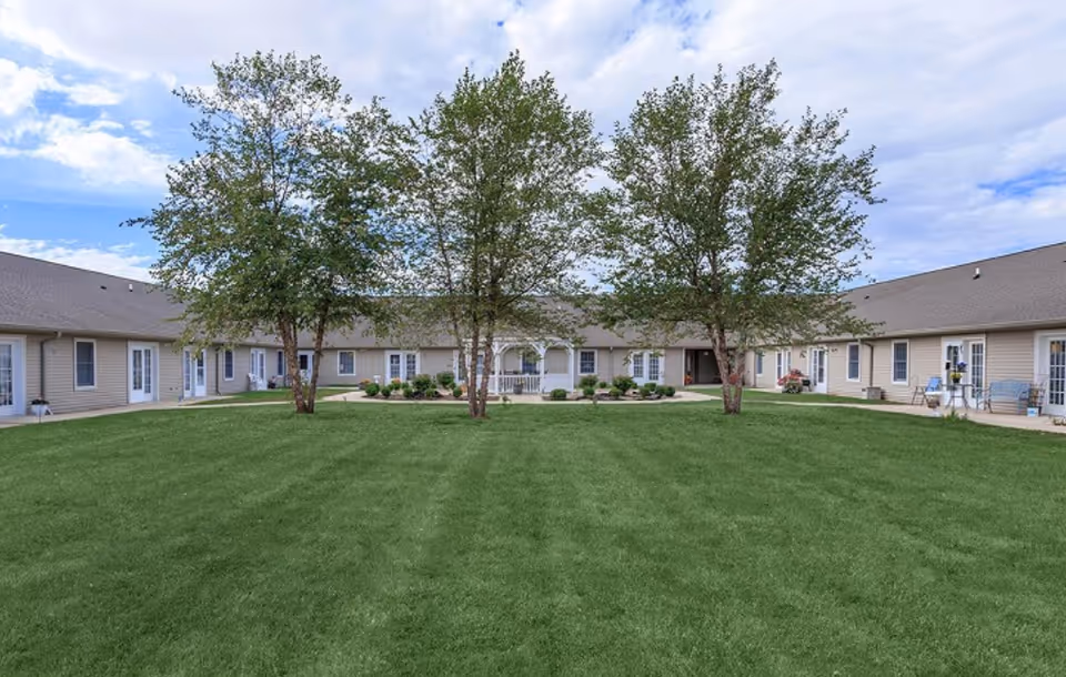 Single-story senior living building surrounding a large grassy courtyard with three trees and a central walkway.