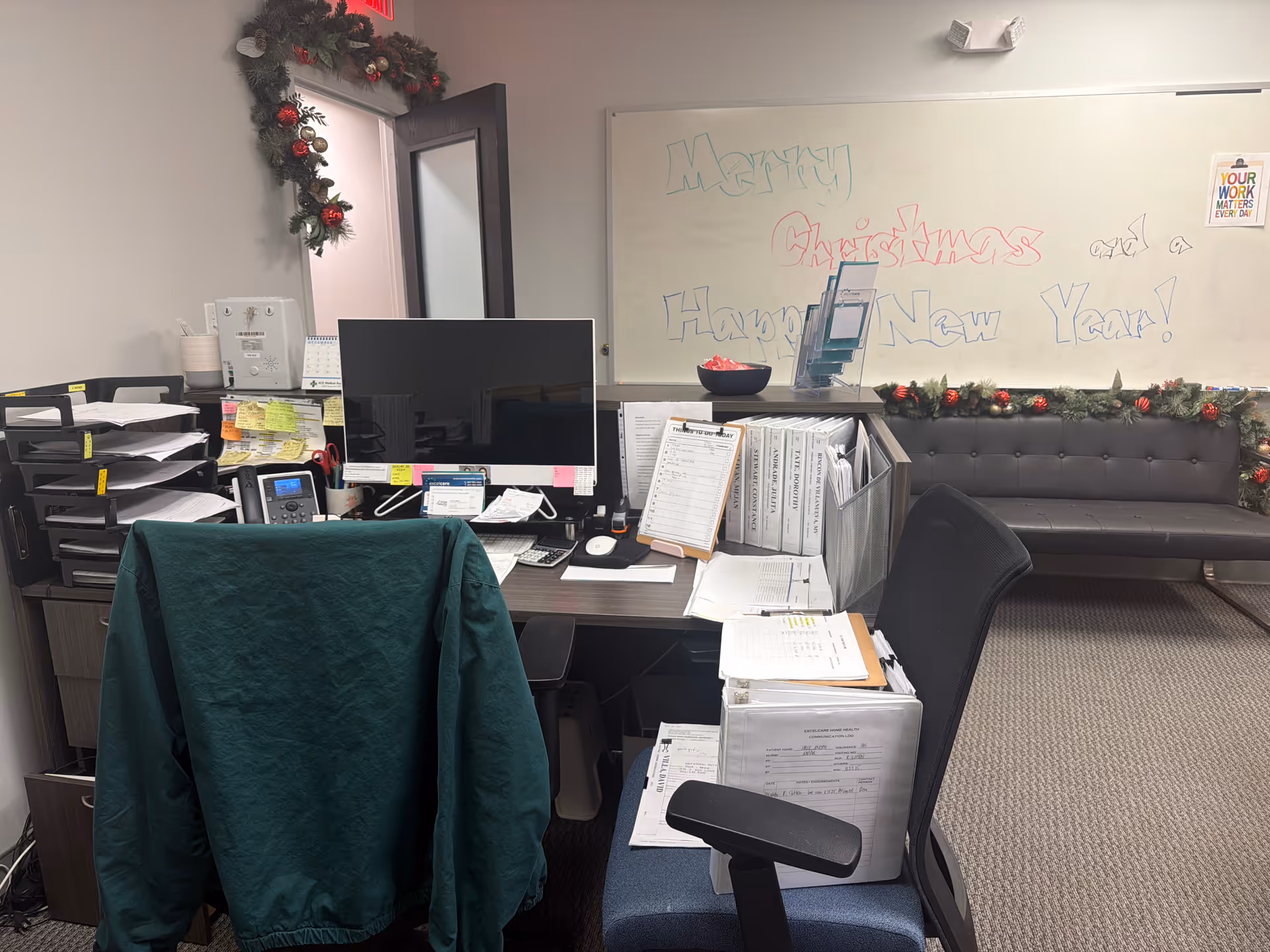 Office workspace with computer, files, holiday garland, and a gray sofa in back.