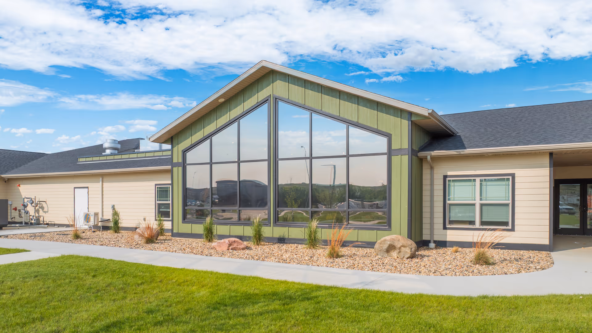 Modern senior living exterior with large glass front, green trim, and landscaping.