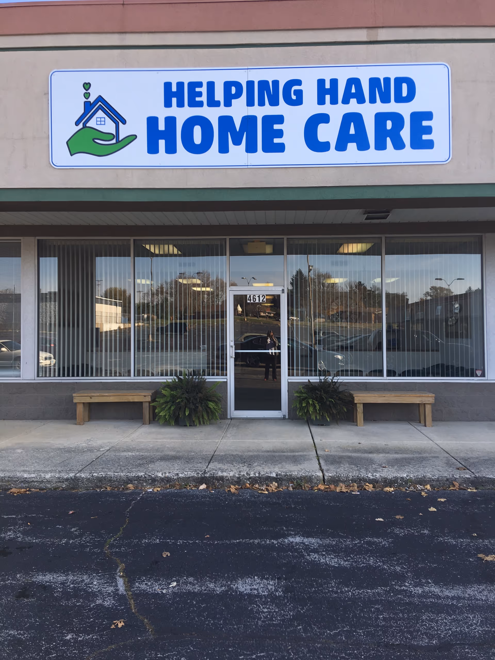 Front view of Helping Hand Home Care storefront with blue sign and glass doors.