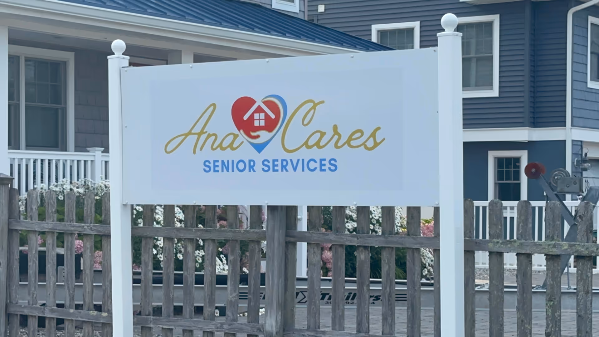 Front view of Ana Cares Senior Services sign with fence and blue building behind
