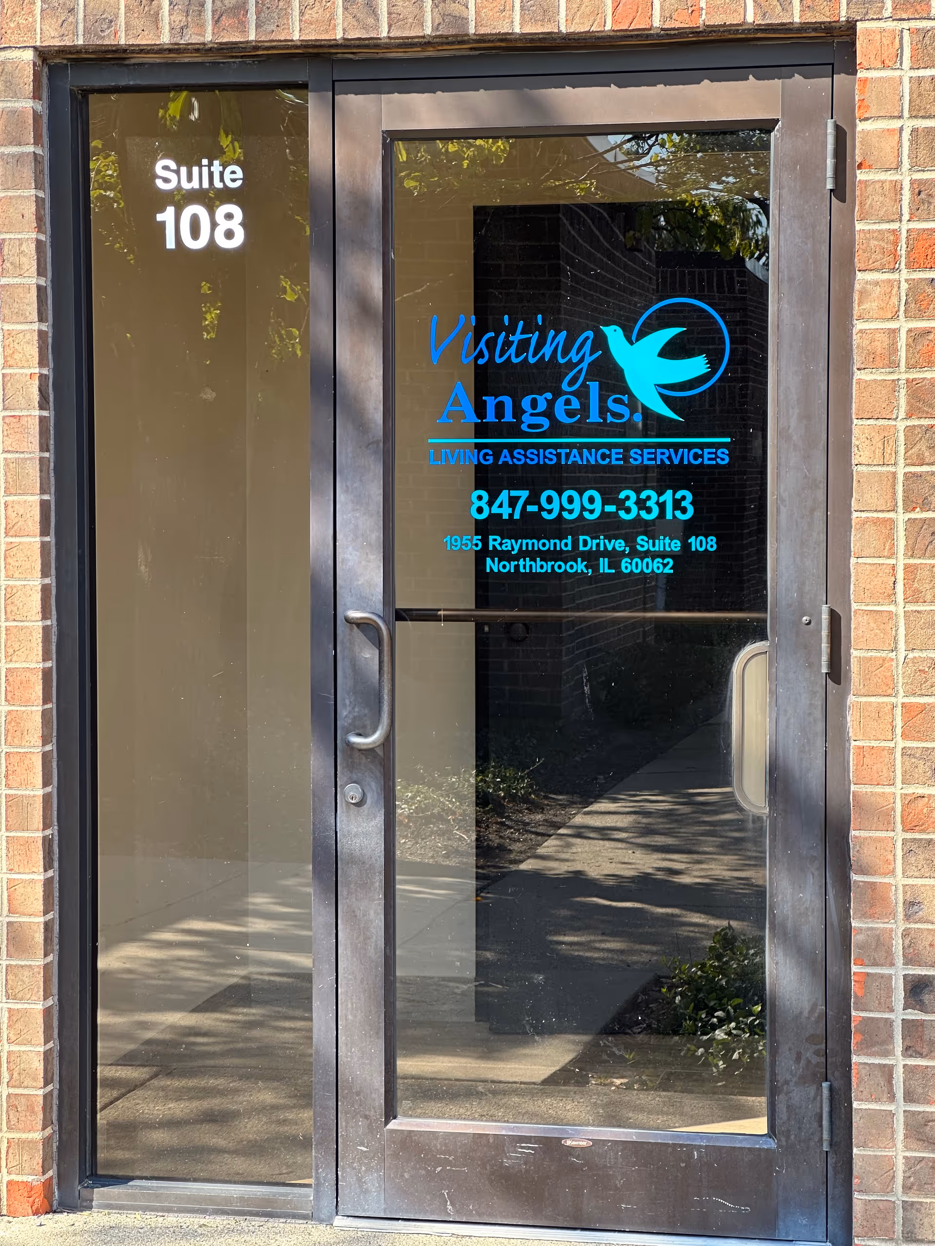 Glass door entrance with Visiting Angels logo and suite 108 on brick exterior.