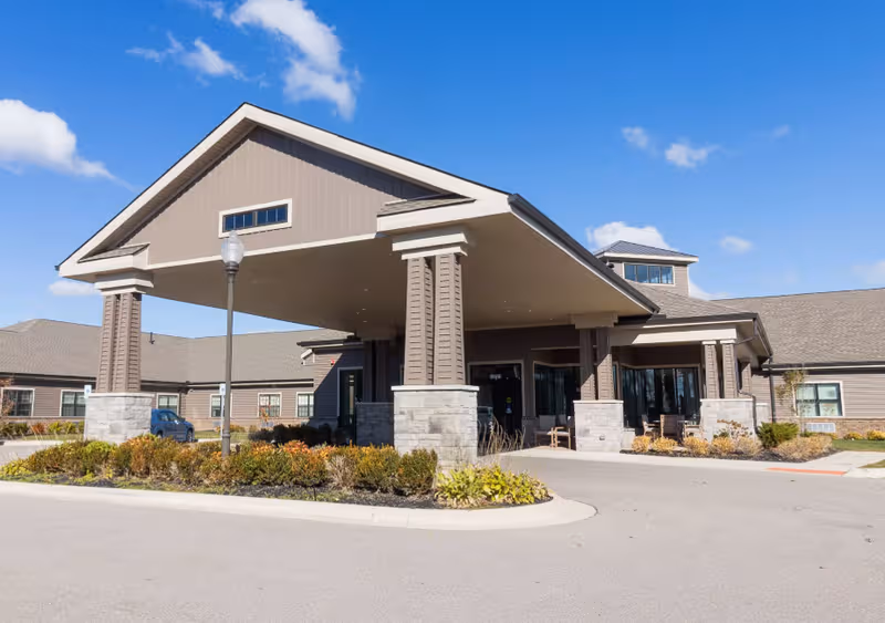 Front view of StoryPoint Brighton senior living facility entrance with porte-cochere and landscaping.