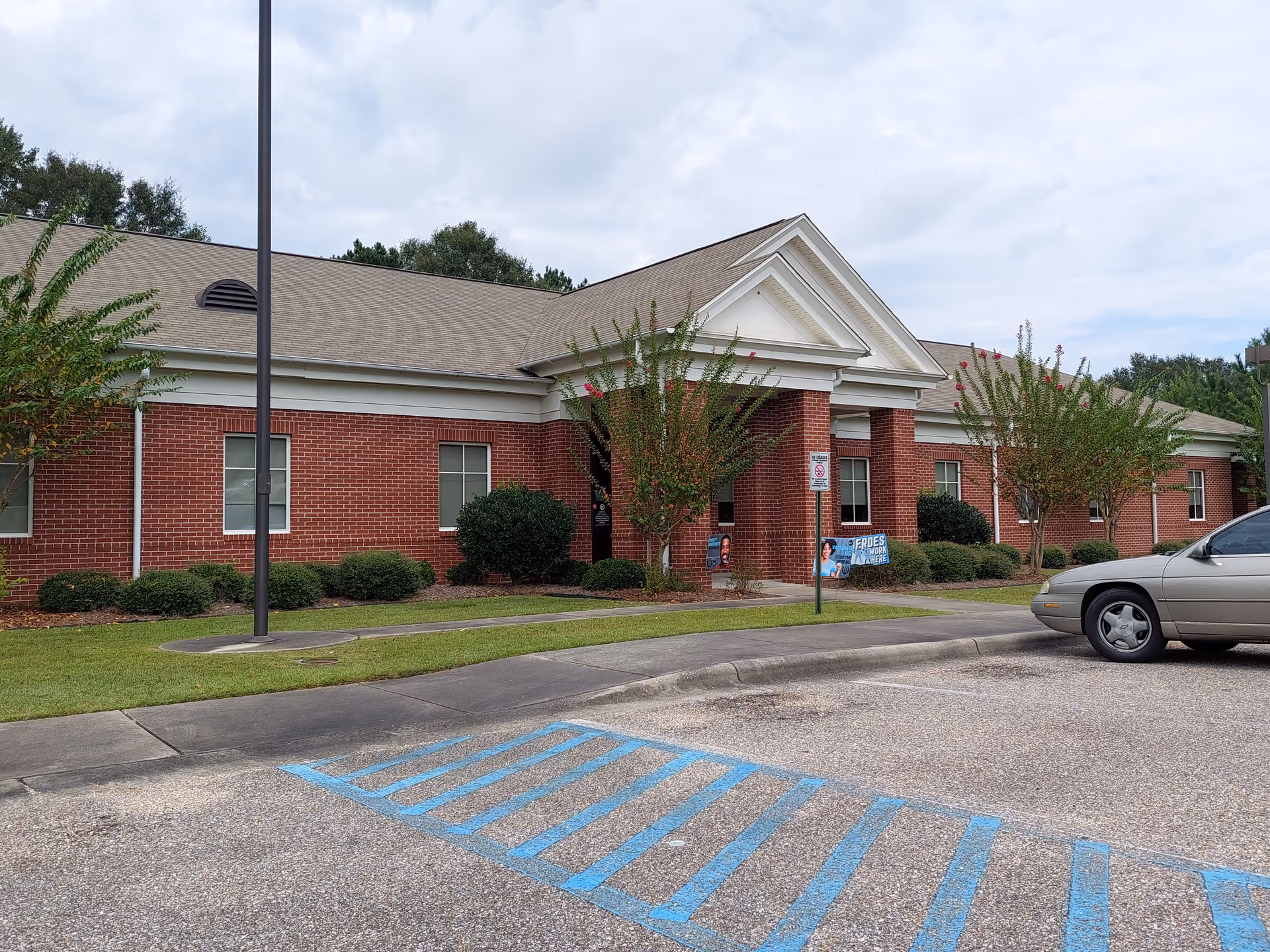 Brick health department exterior with a white-trim entrance and landscaped shrubs.