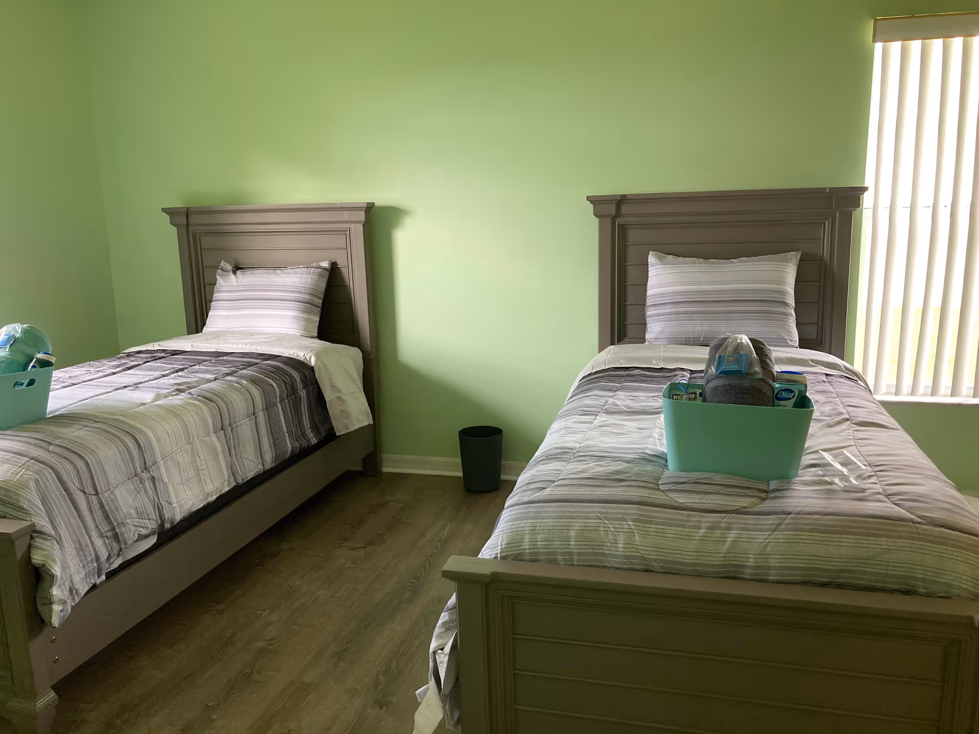 Two twin beds with striped bedding in a lime-green bedroom, wooden headboards, window with blinds.