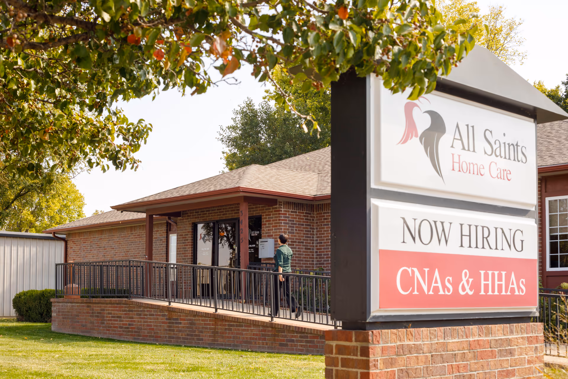 Exterior of All Saints Home Care with a large Now Hiring sign and brick building