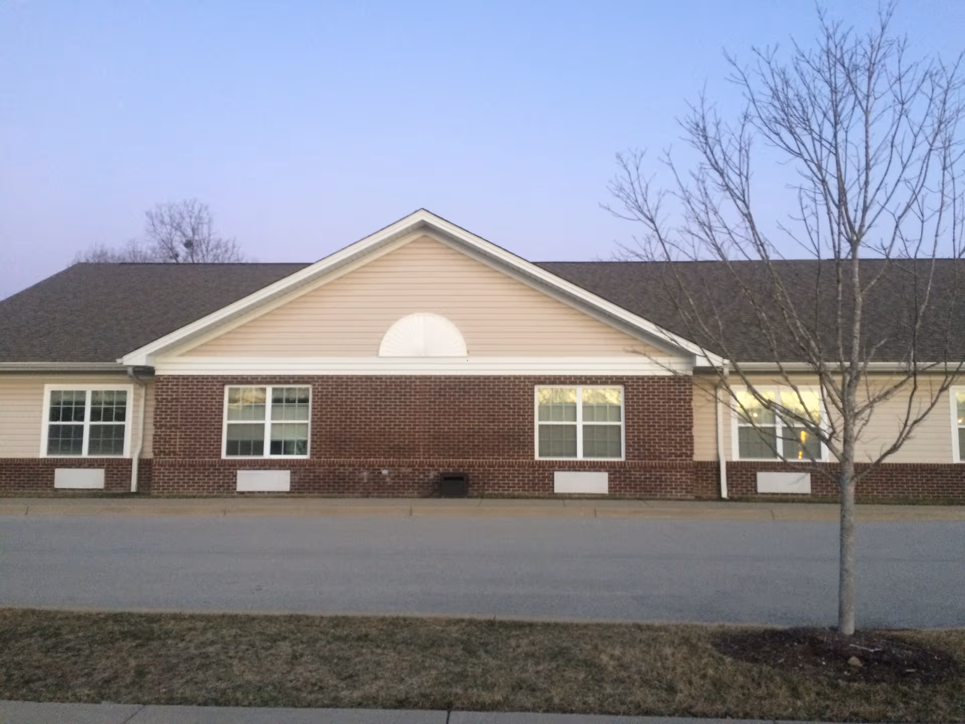 Exterior view of a single-story brick-and-beige senior facility with windows and a bare tree.