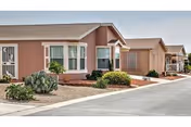 Front exterior of pastel-colored senior living building with landscaped shrubs and a paved driveway.