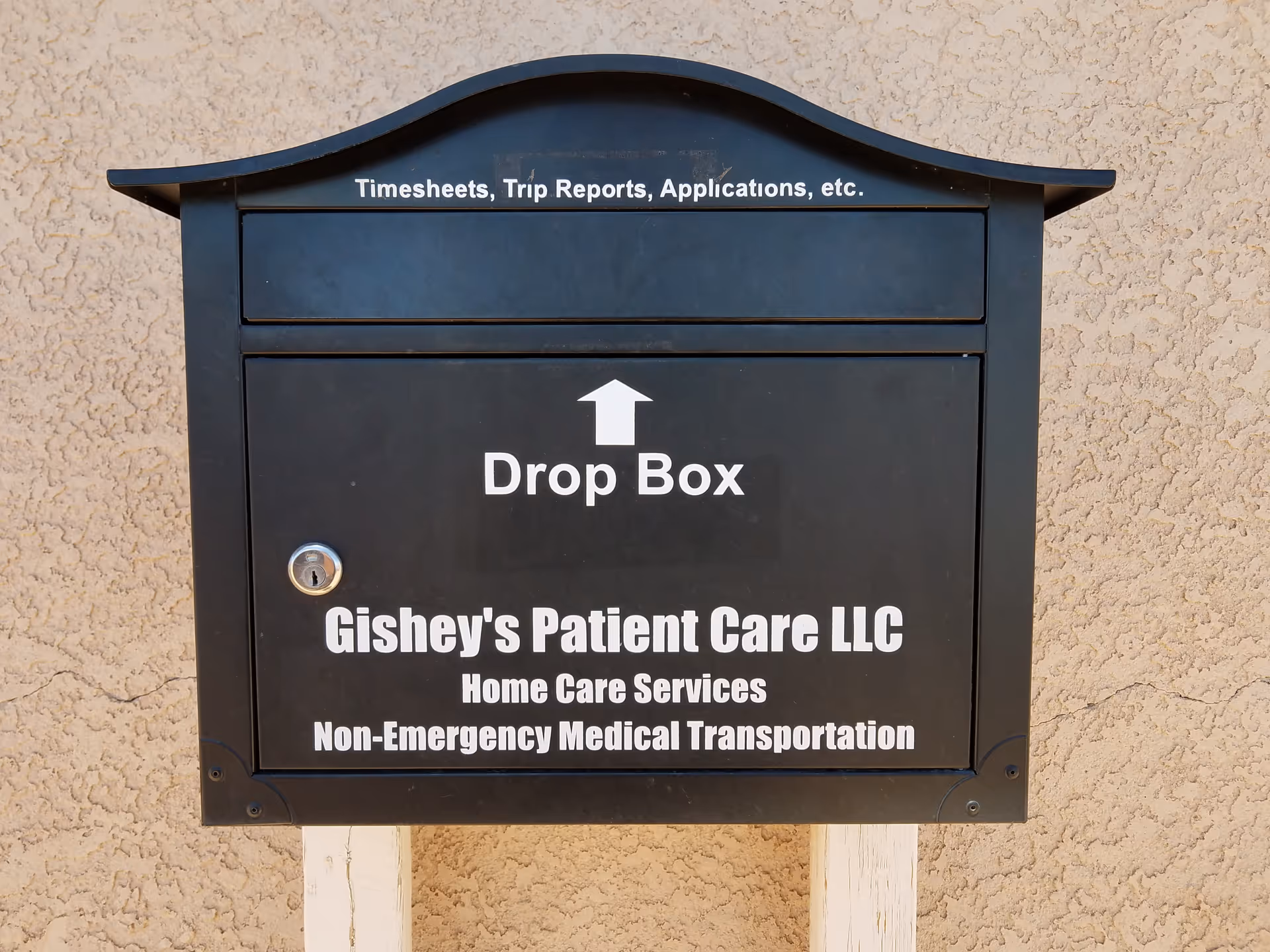 Exterior black drop box with Gishey's Patient Care LLC signage on a stucco wall.