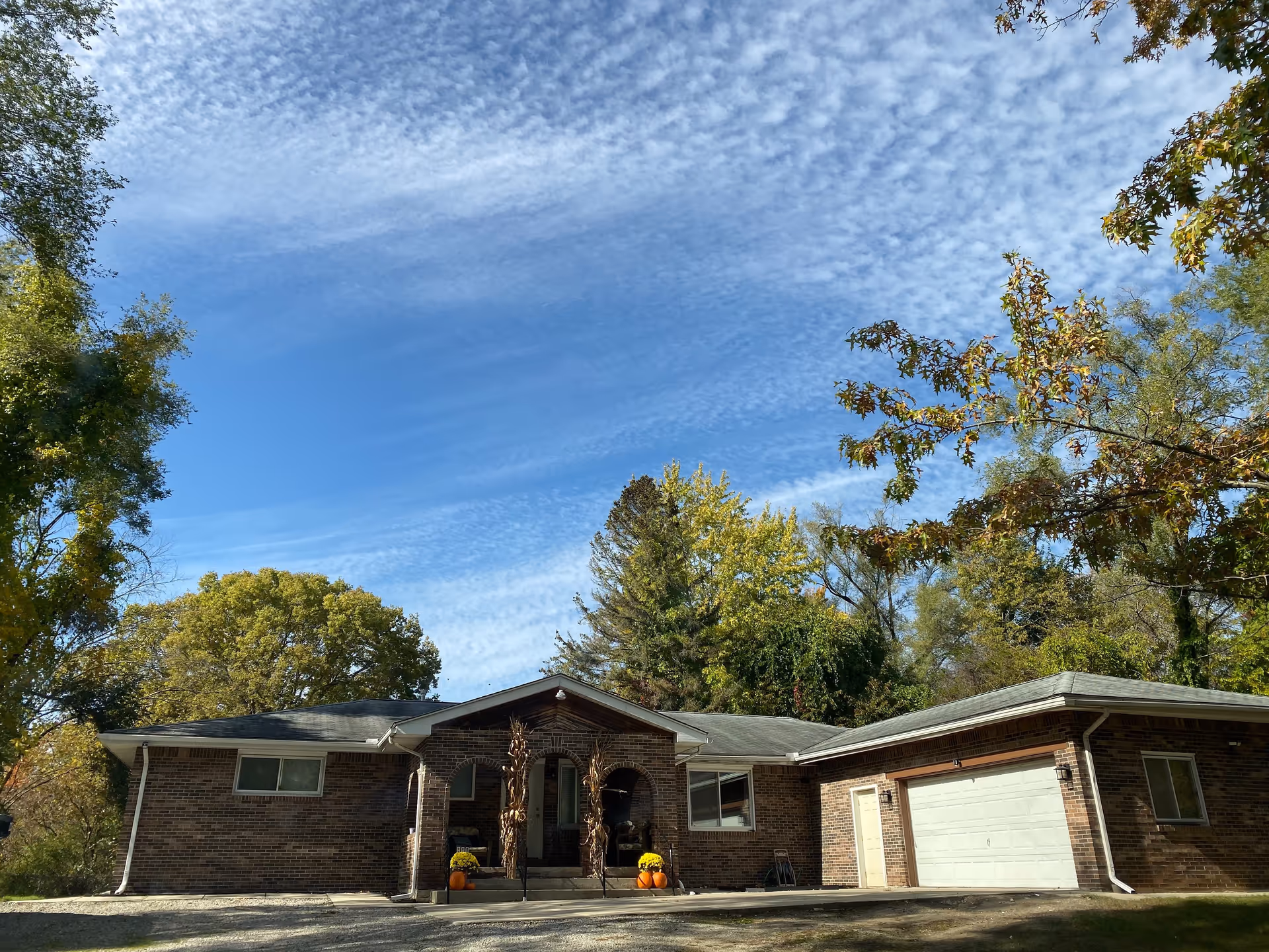 Single-story brick building with an attached garage and a front entrance flanked by potted plants, surrounded by trees under a blue sky.