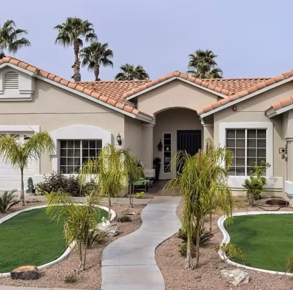Sunny beige senior living facility with tiled roof, curved walkway, and palm trees.