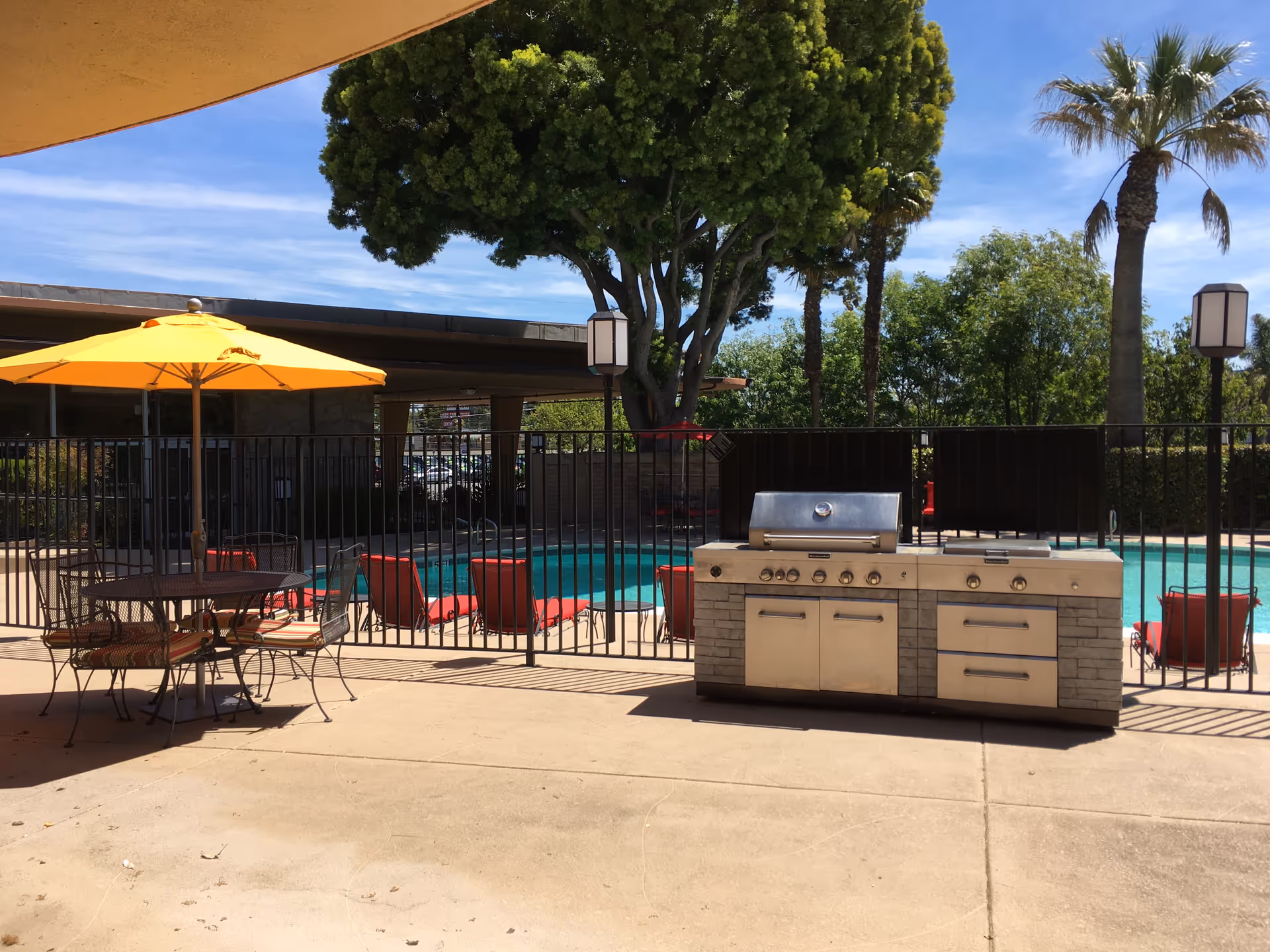 Outdoor pool area with a grill station, patio furniture, and a yellow umbrella.