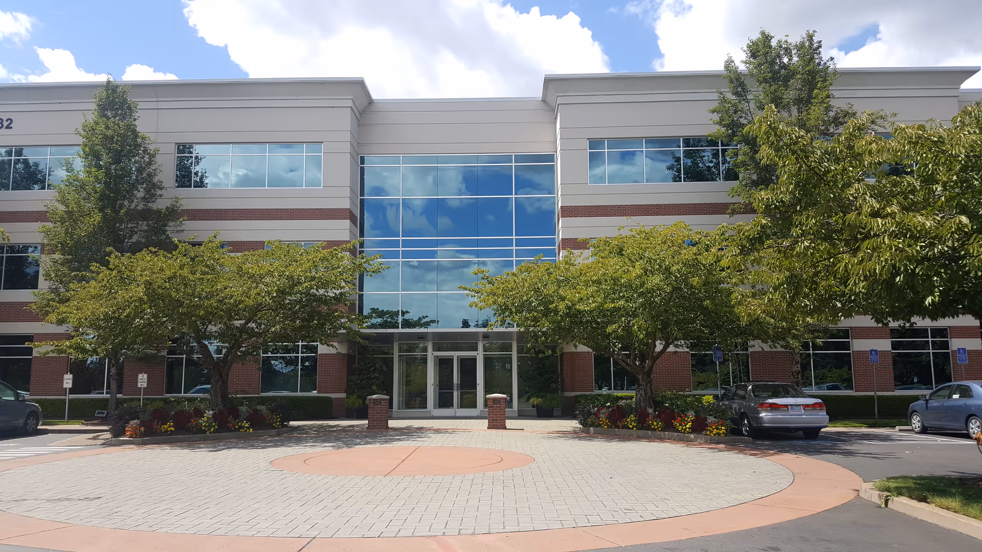 Modern building exterior with glass entrance, trees, and parked cars.