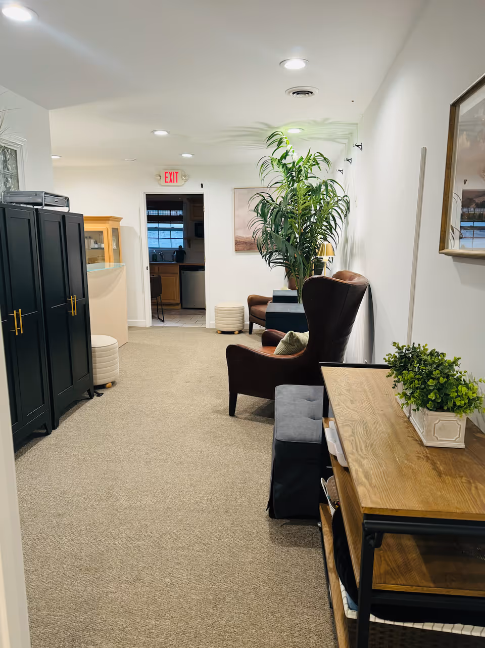 A well-lit senior living hallway with seating, plants, and a small office area.