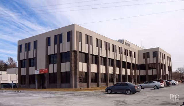 Exterior view of a large brick and beige four-story building with a parking lot.