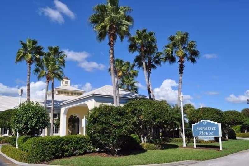 Exterior view of Somerset House at Oak Harbor with palm trees and a blue sign.