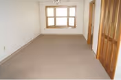 An empty room with beige carpet, white walls, a window, and wooden doors.
