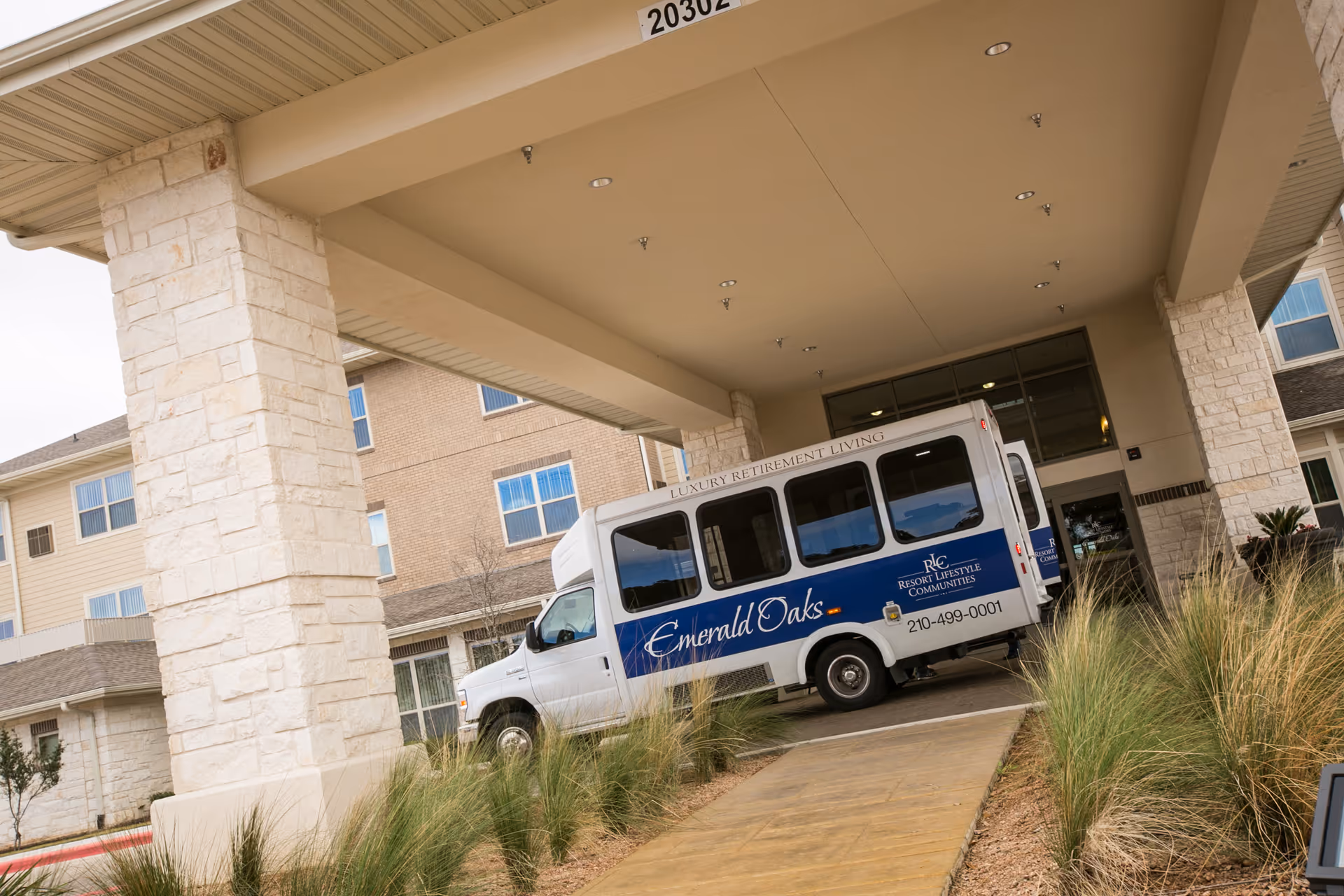 Front view of Emerald Oaks Retirement Resort entrance with a blue shuttle bus parked under canopy.