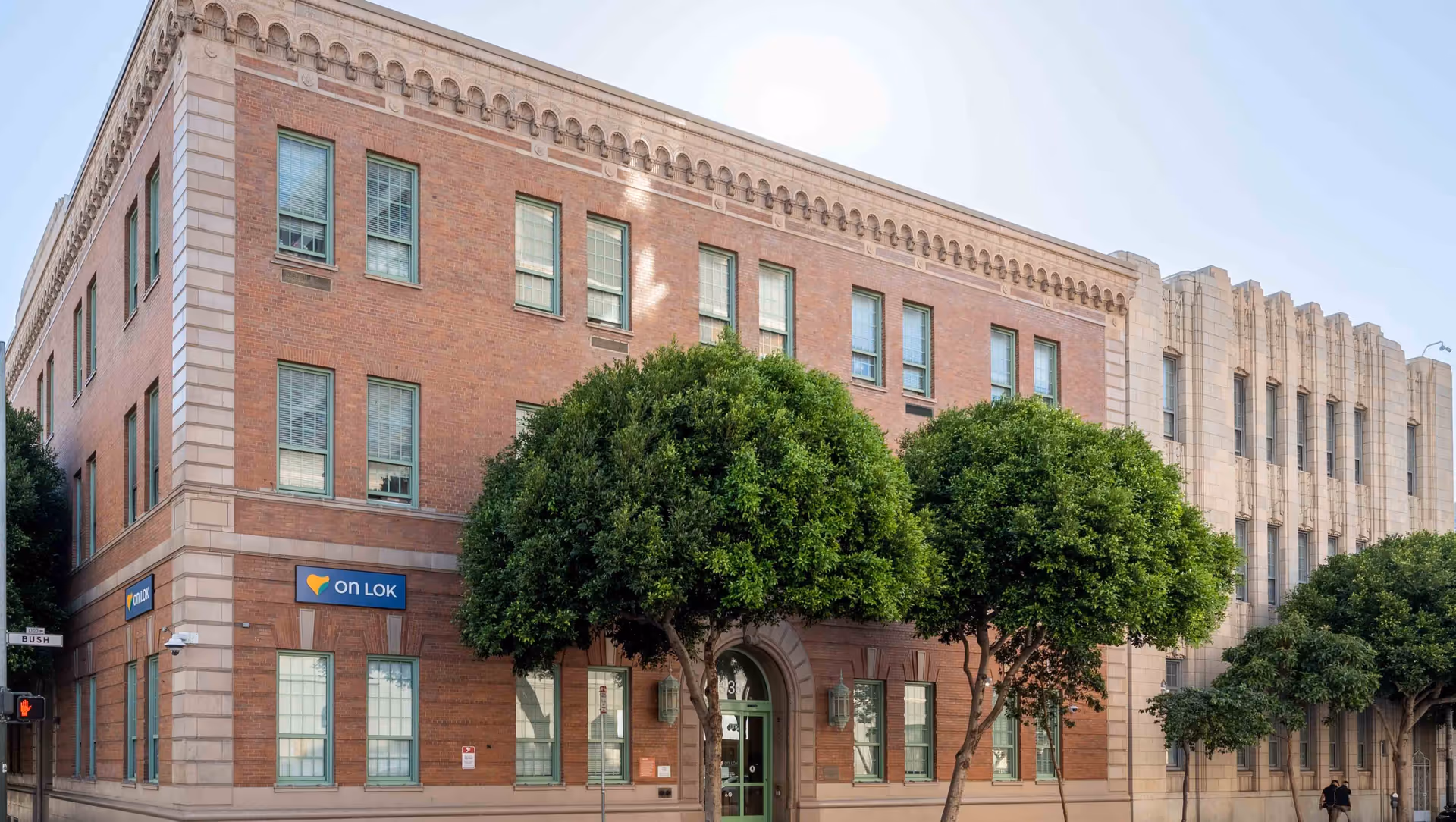 Brick building of On Lok PACE Gee Center with an arched entrance and trees.