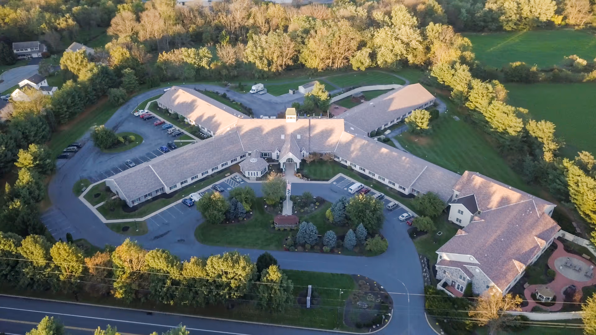 Aerial exterior view of a large X-shaped senior living facility with parking, driveways, and surrounding trees.