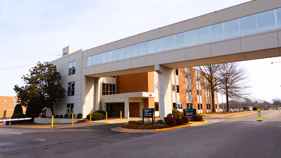 Modern medical building exterior with a glass-walled upper corridor and covered entrance.
