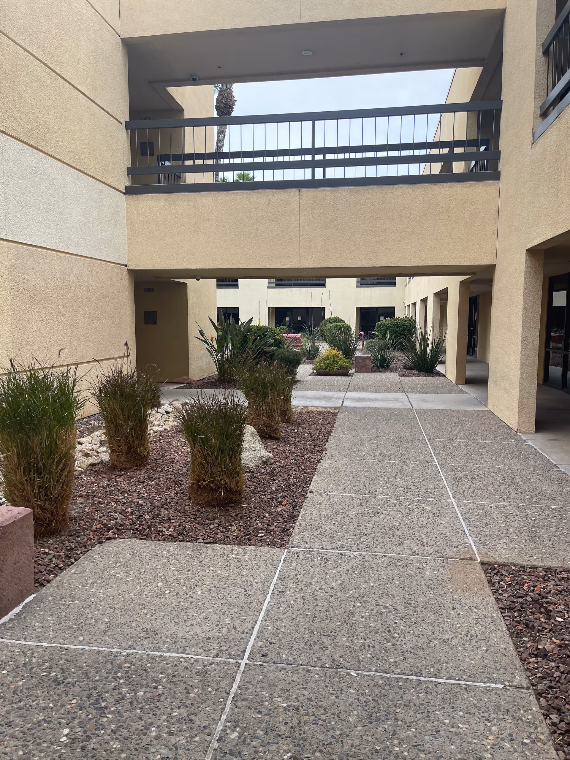 Outdoor courtyard of Valley Wise Home Care LLC with beige buildings, walkway, and drought-tolerant plants.