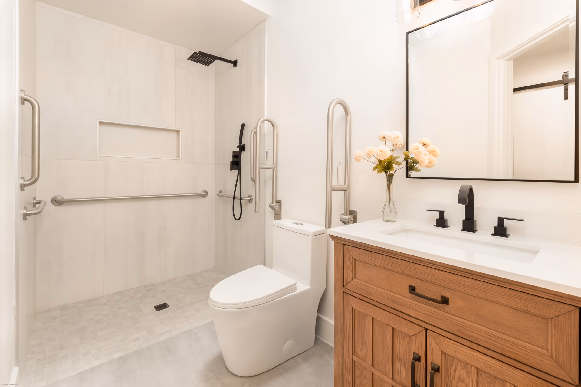 Accessible bathroom with walk-in shower, grab bars, toilet, and wooden vanity in a senior living facility.
