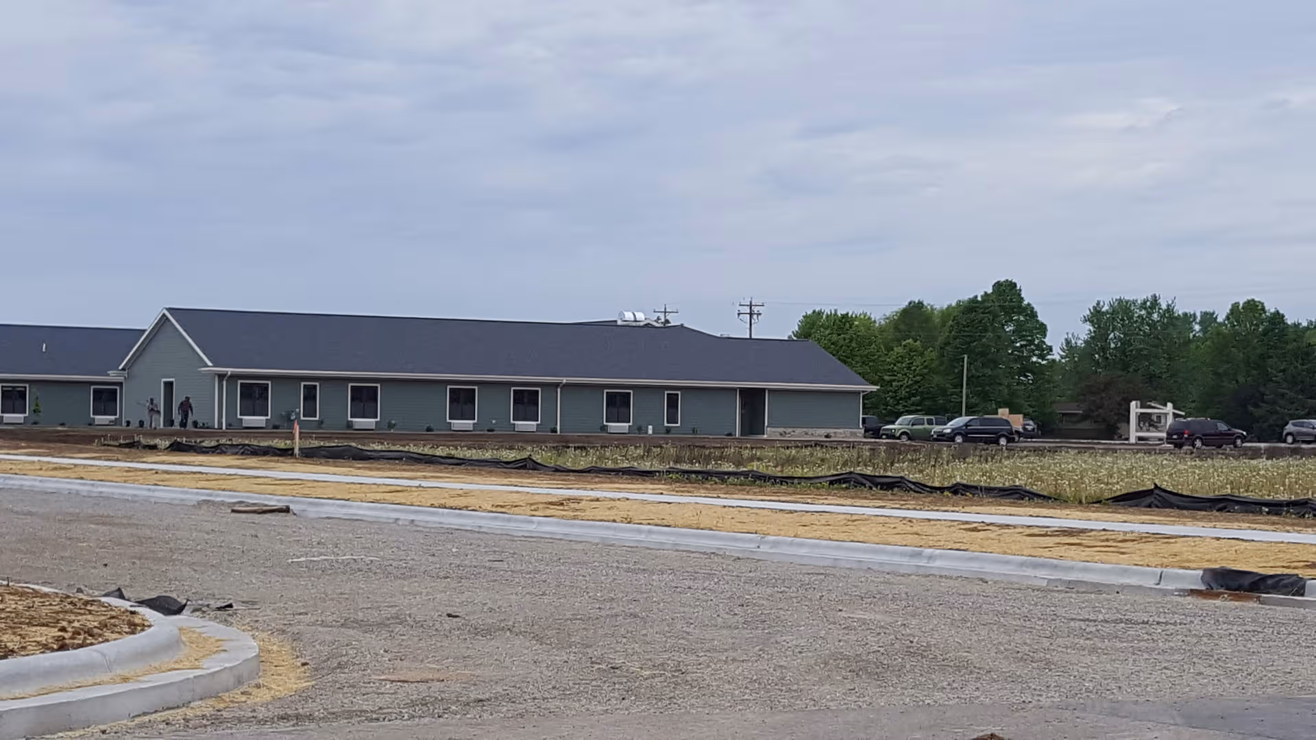 Exterior view of a single-story assisted living facility with blue-gray siding and a parking lot.