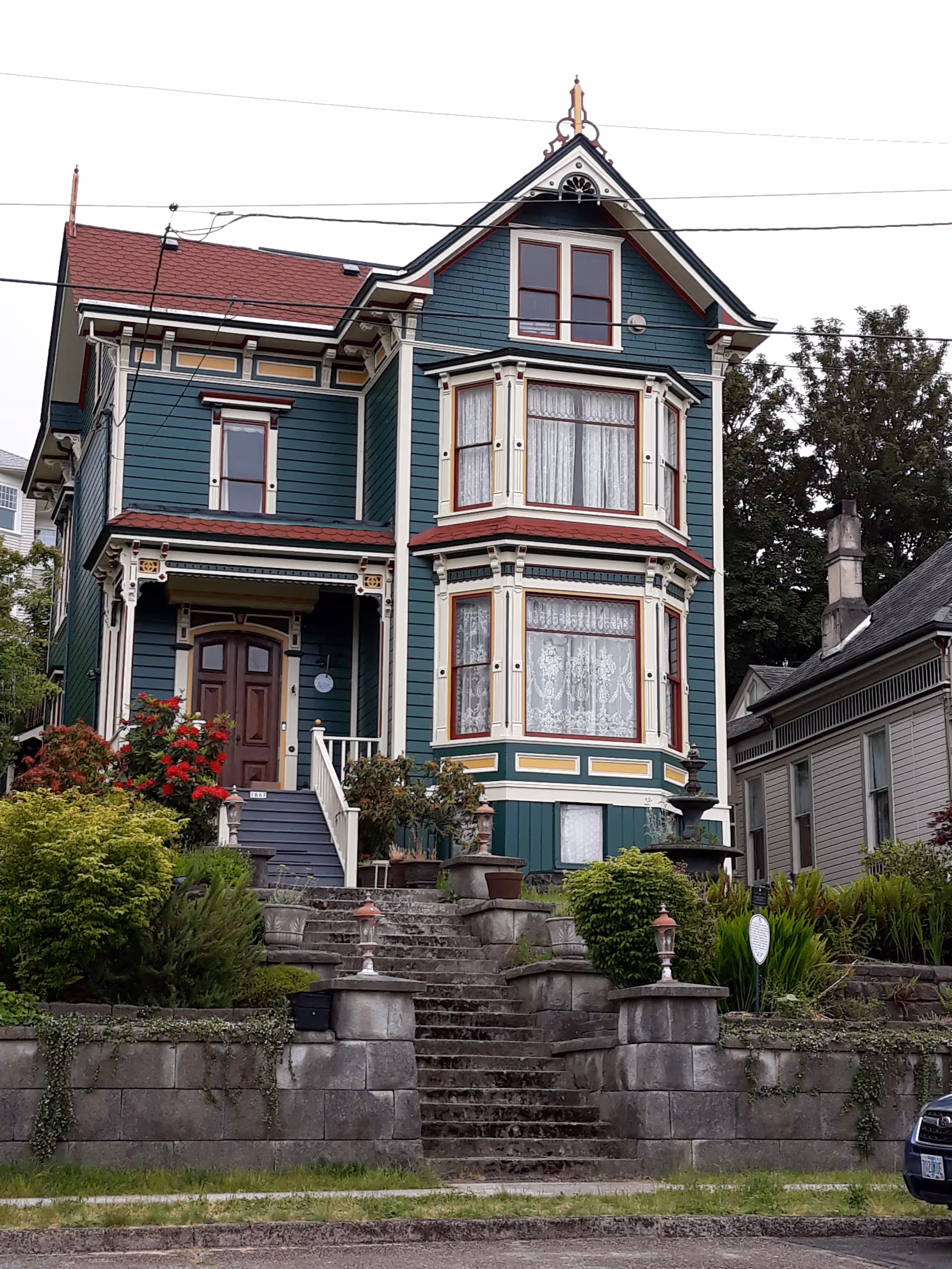A Victorian-style house with ornate trim, front steps, and lush garden.