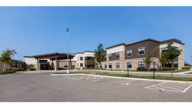 Exterior view of a modern senior living facility with a covered entrance and parking lot.