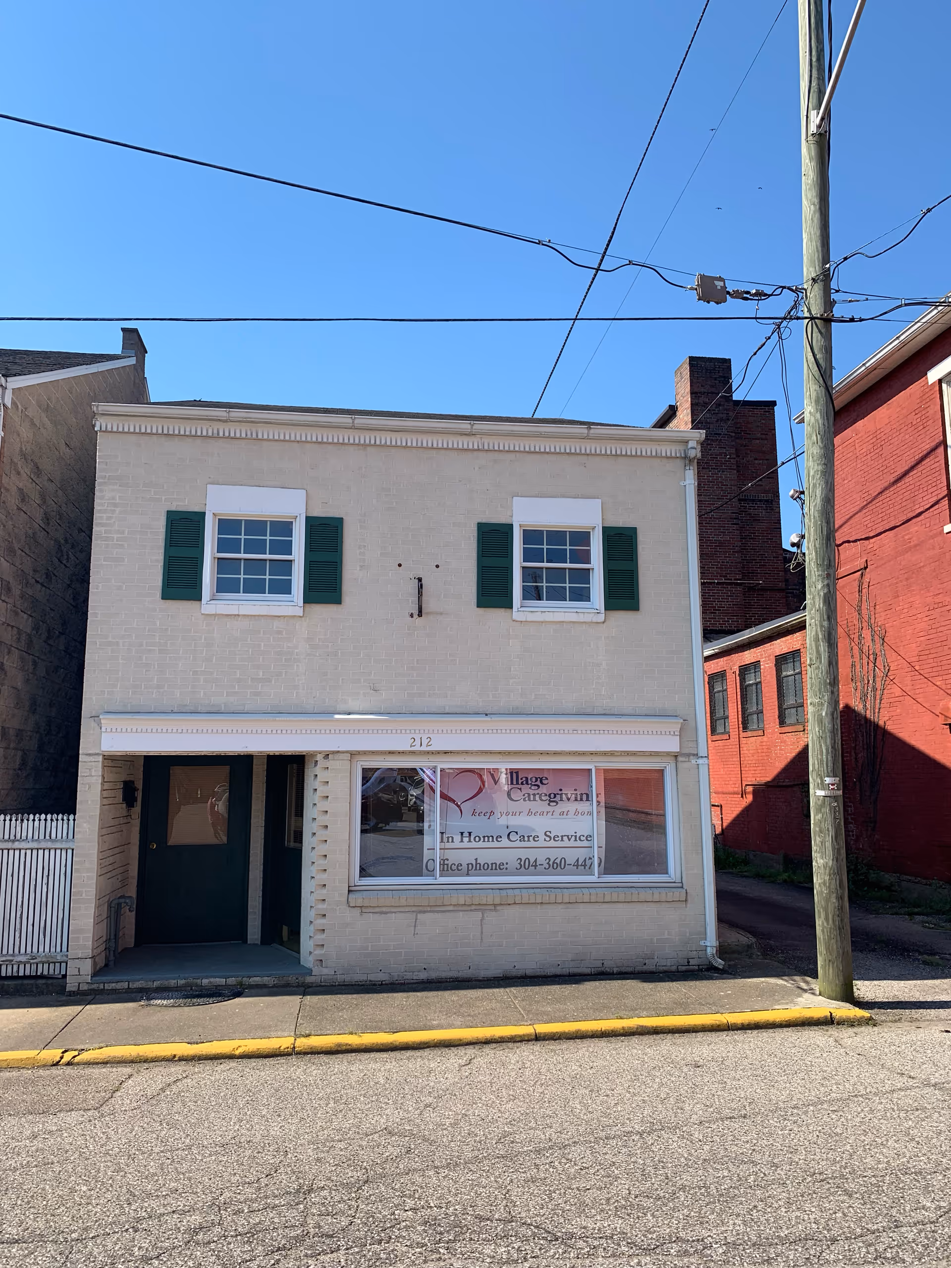 Two-story white brick building with green shutters and a Village Caregiving sign.
