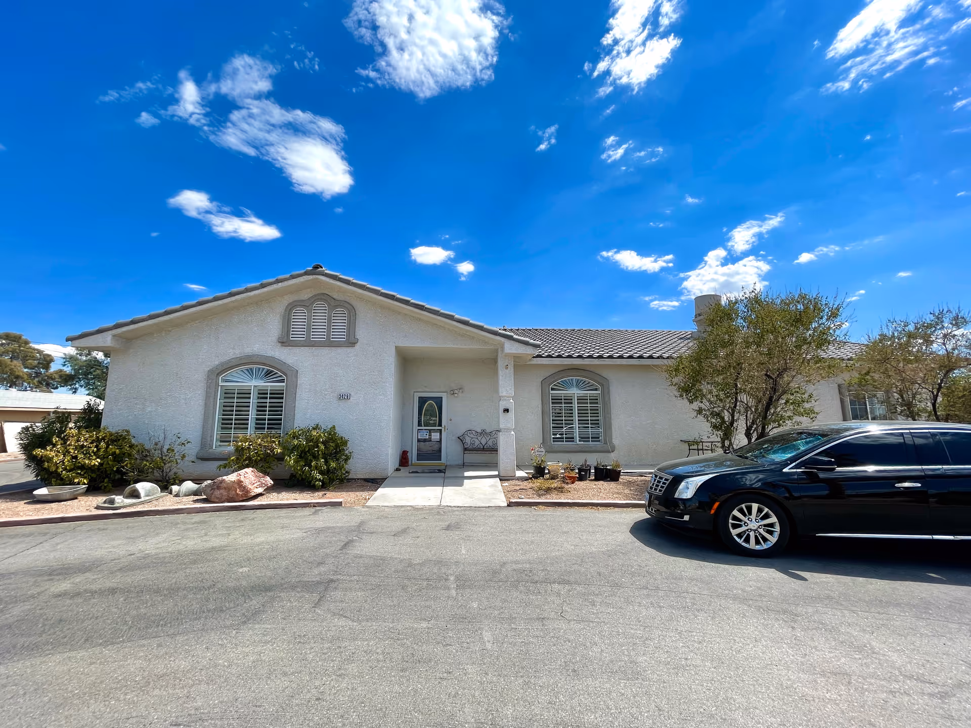 Single-story stucco home with arched windows and a central front entrance, landscaped frontage and a black car parked in front under a bright blue sky.
