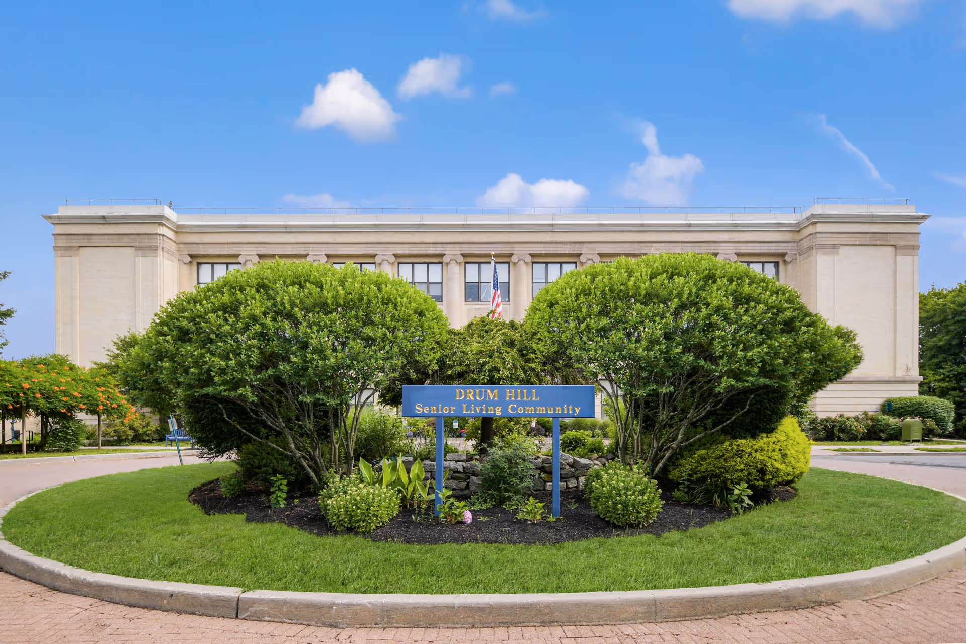 Exterior view of Drum Hill Senior Living Community with manicured landscaping and sign.