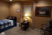 Cozy bedroom in an assisted living facility with bed, lamp, and seating area.