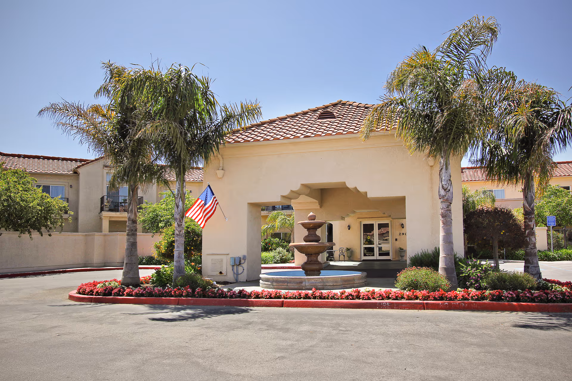 View of a senior living facility entrance with palm trees and a fountain.