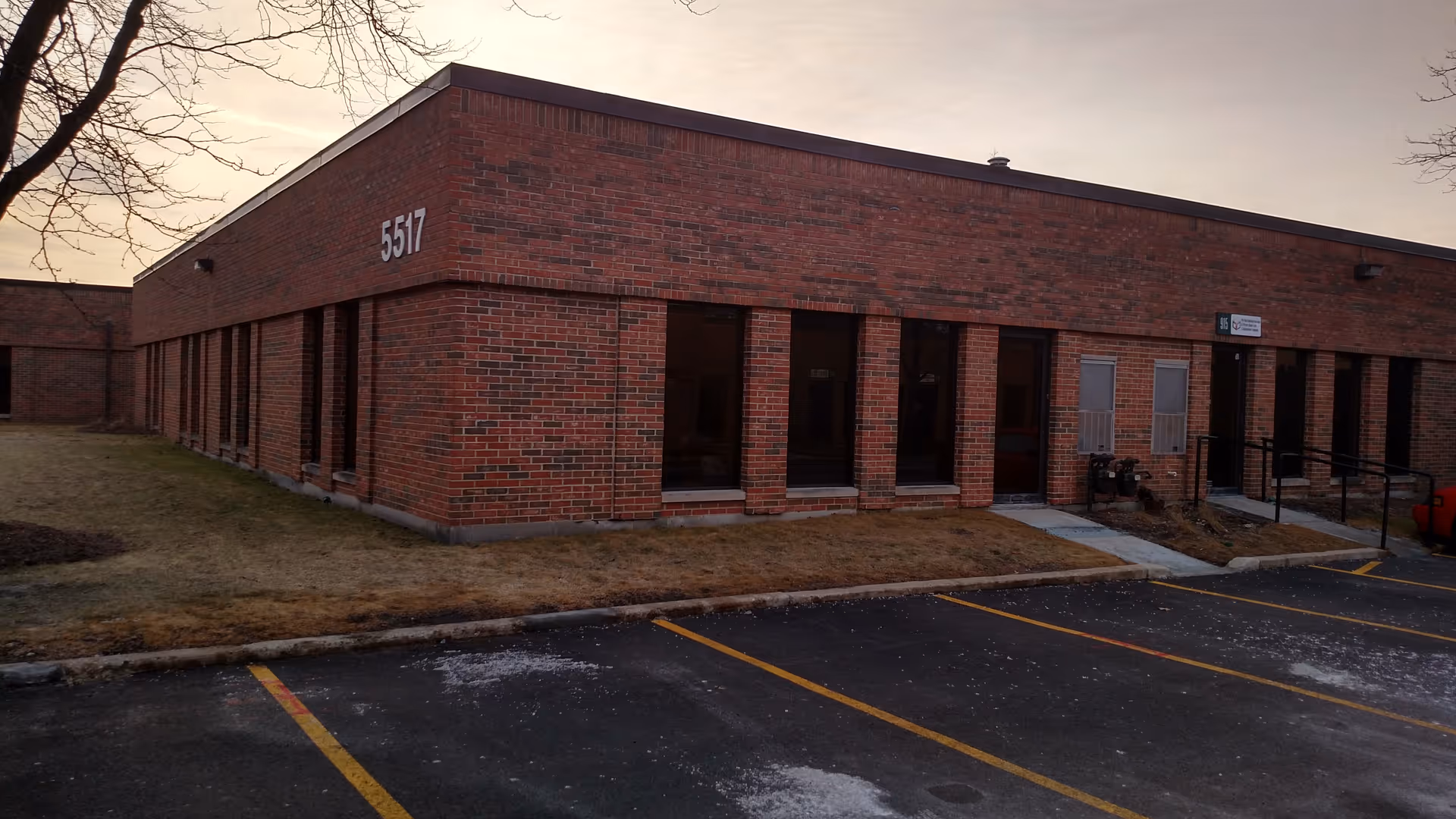 Exterior brick building facade with multiple windows and a parking lot in front.