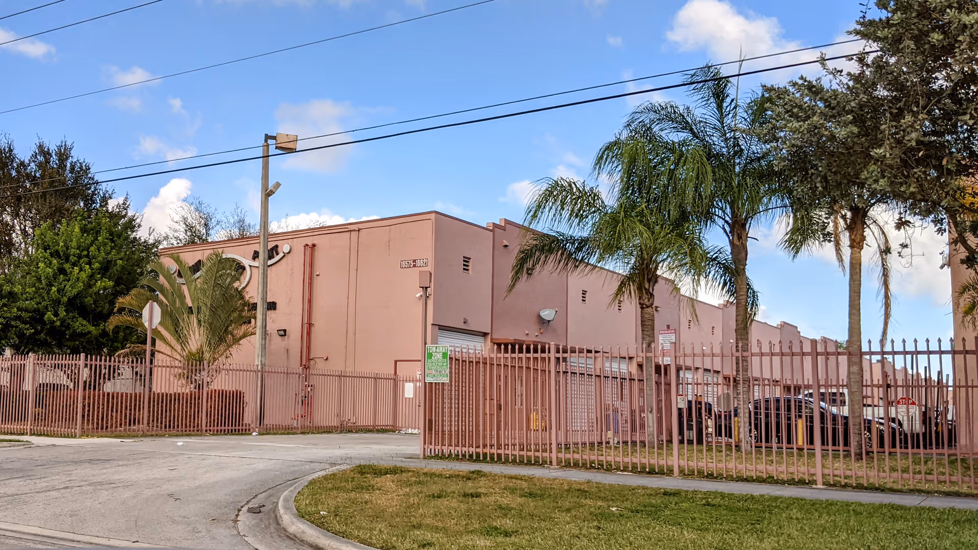 Exterior view of a pink senior living facility behind a tall metal fence.