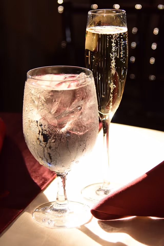 Two glasses of drinks on a lit dining table with red napkin.