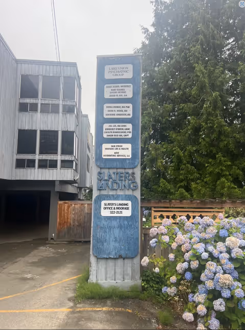 Tall blue signboard with multiple business names beside a building exterior and hydrangea flowers.
