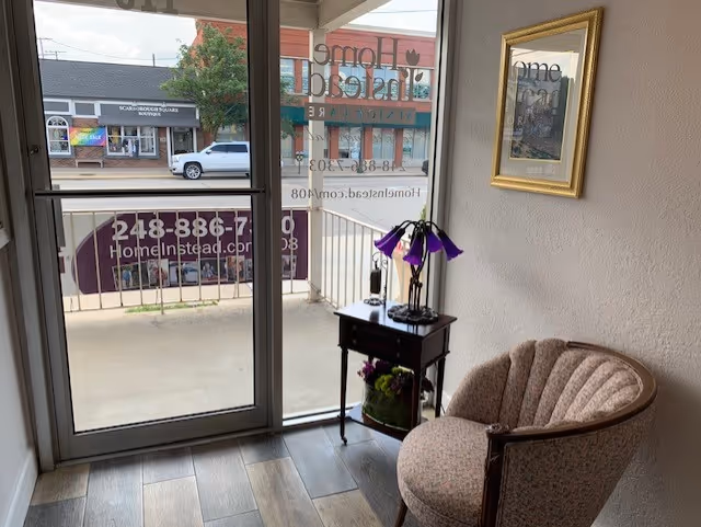 A small seating nook beside a glass door, featuring a side table, lamp, and framed art.