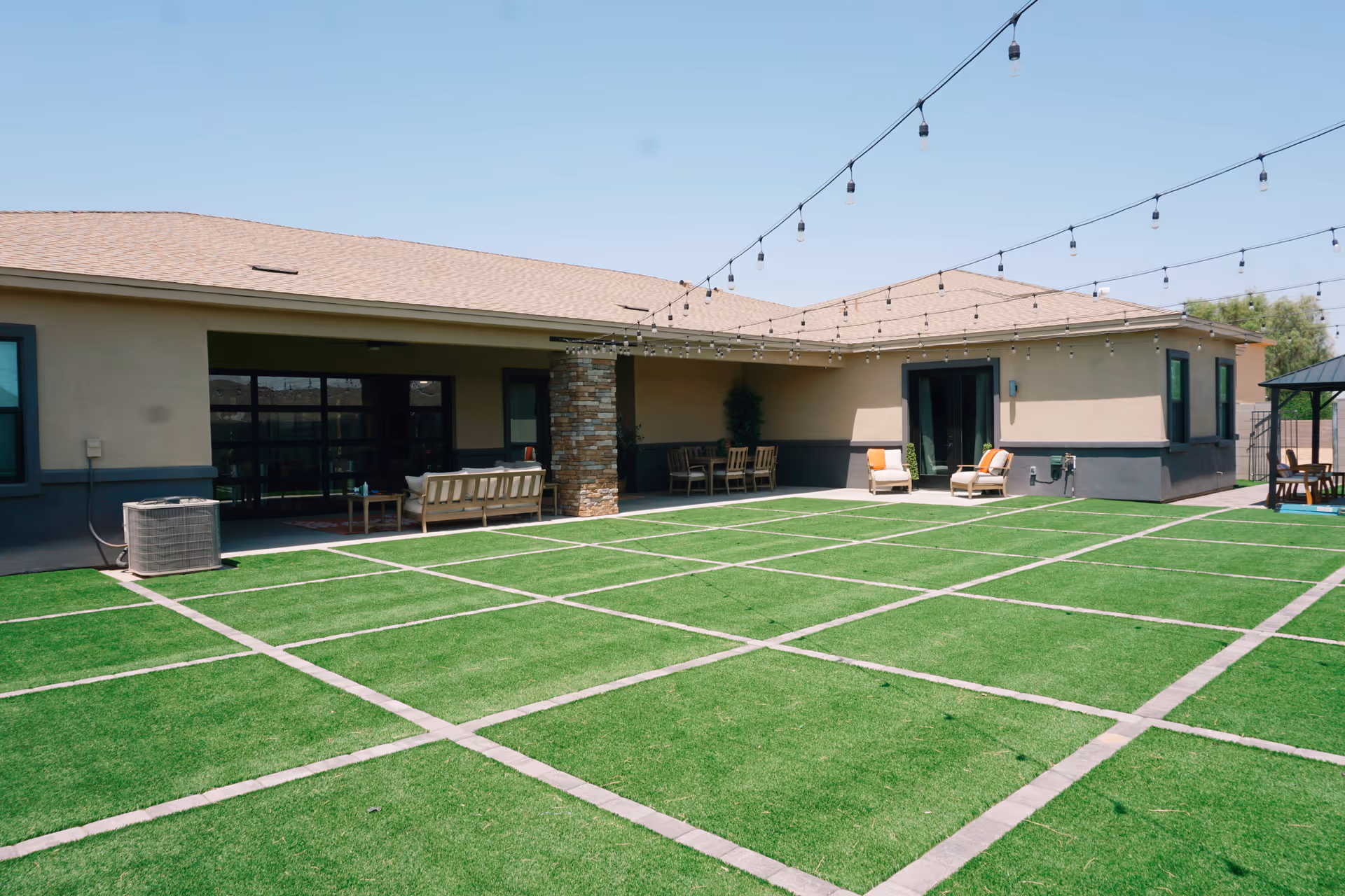 Single-story senior living facility with outdoor seating, string lights, and a grassy, grid-patterned patio.