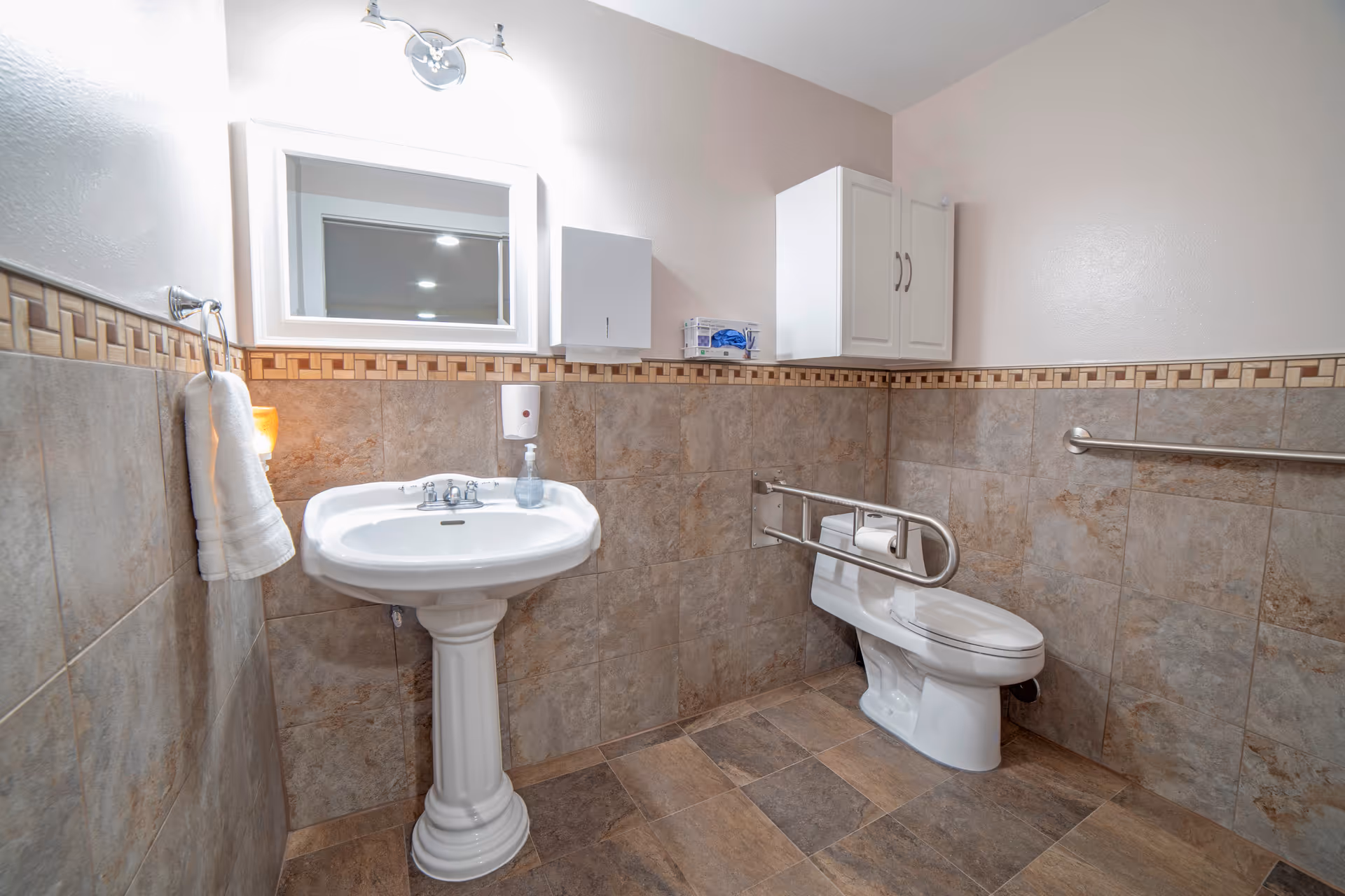 Accessible bathroom with pedestal sink, toilet, grab bar, mirror, and tiled walls.