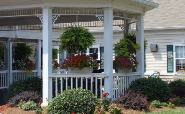 White porch columns with hanging baskets and lush plants in front of a beige building.