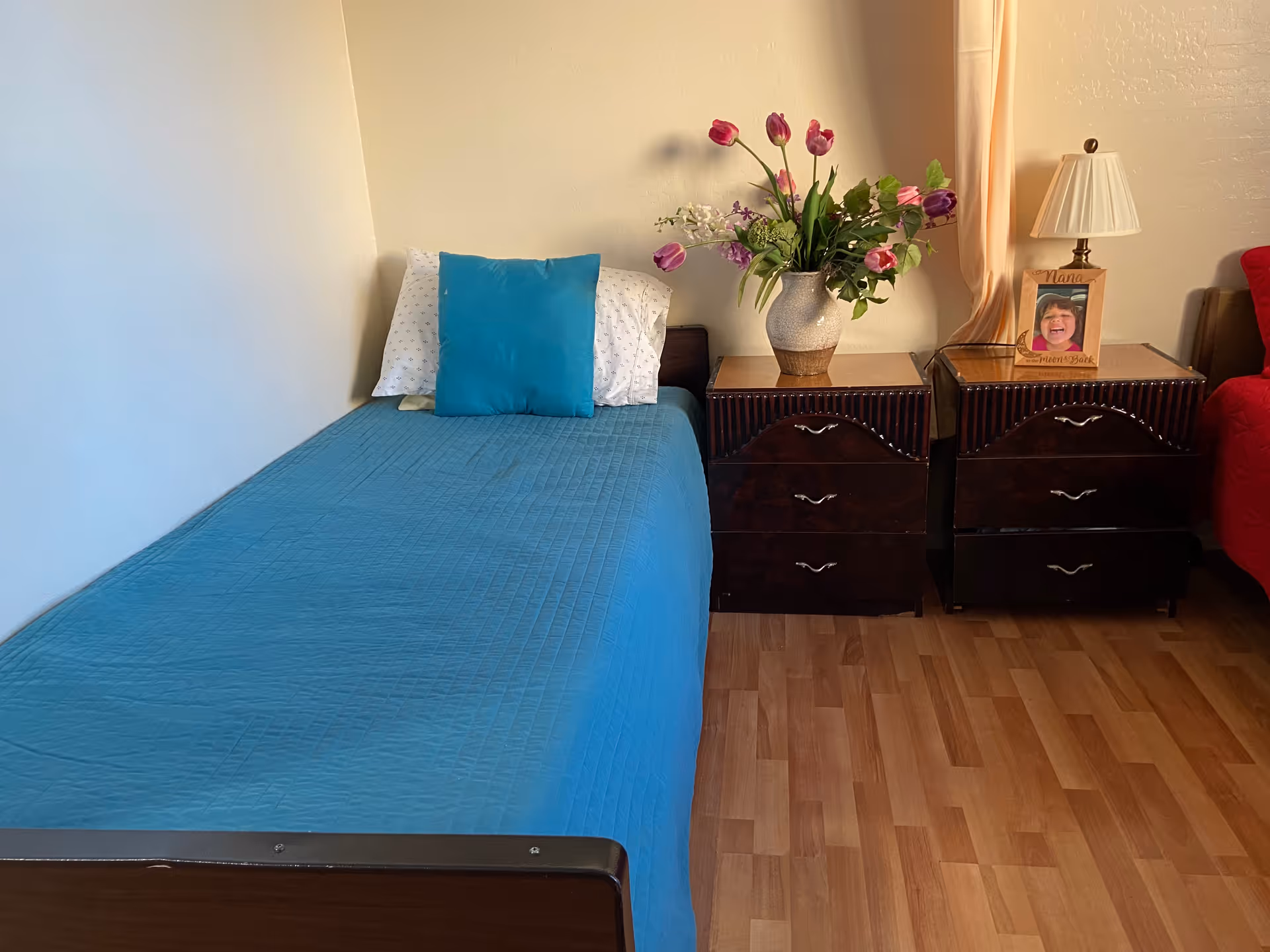 Bedroom with a blue bedspread, two dark nightstands, flowers, and a framed photo.